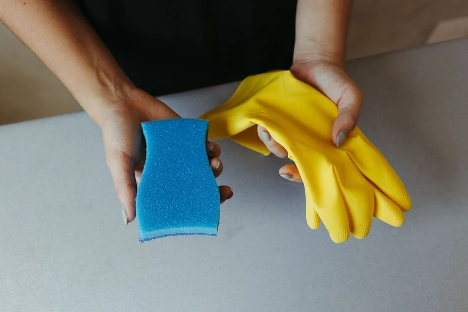 Detailní záběr na ruku čistící venkovní okno stěrkou v žlutých rukavicích.